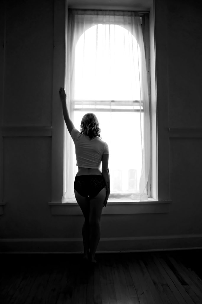 Woman in white tshirt and underwear standing in front of a window, arm raised Chicago Boudoir