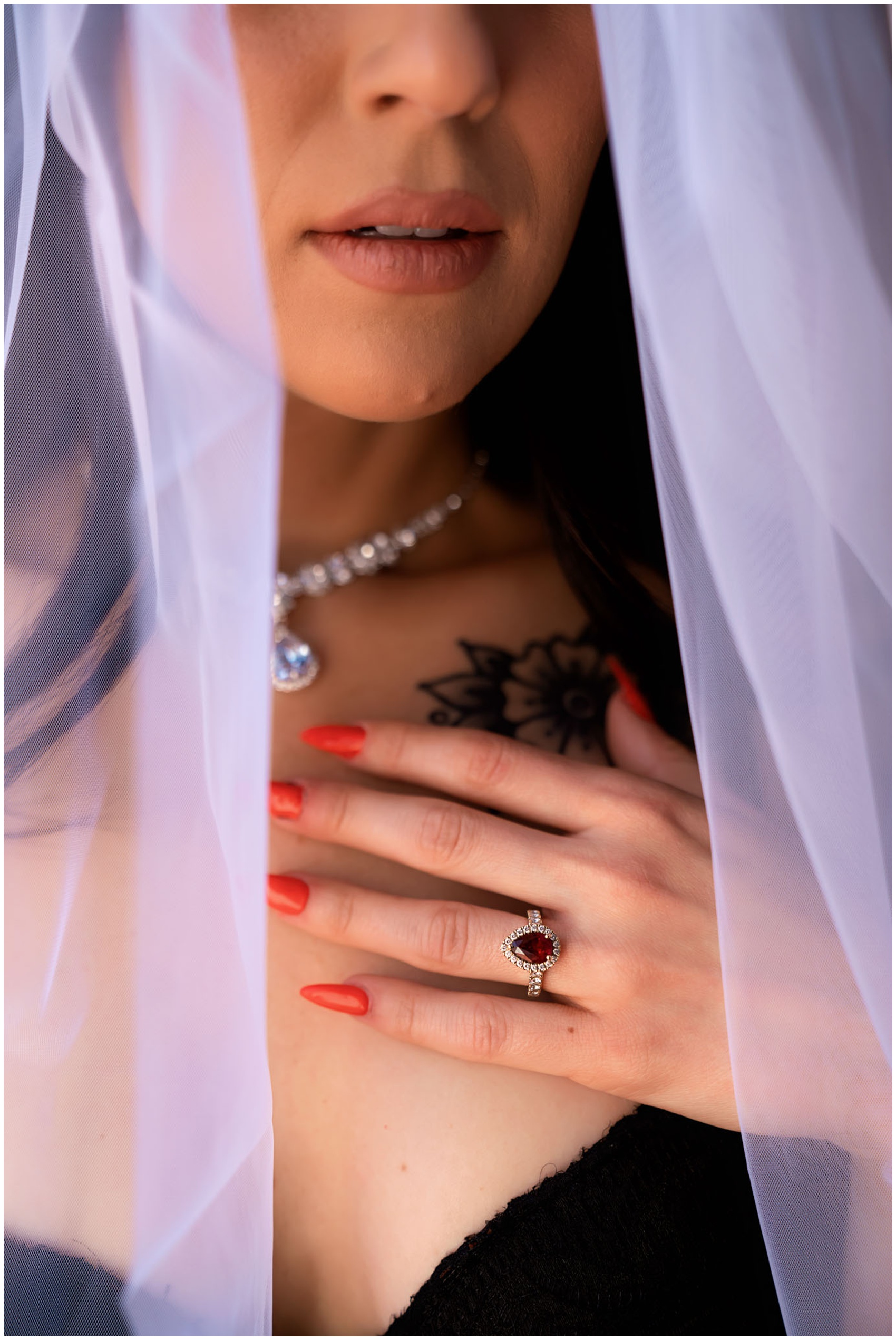 A woman stands in her veil with her ring hand on her chest in black bra