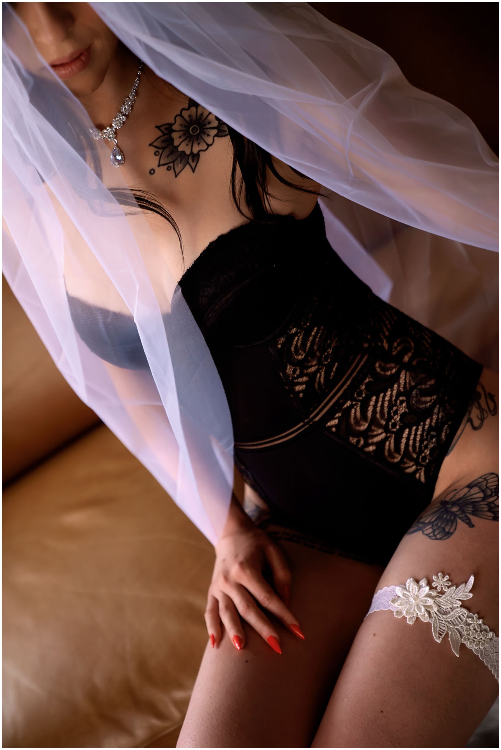 A woman sits on a leather couch in black lingerie and a veil after visiting bridal shops elgin