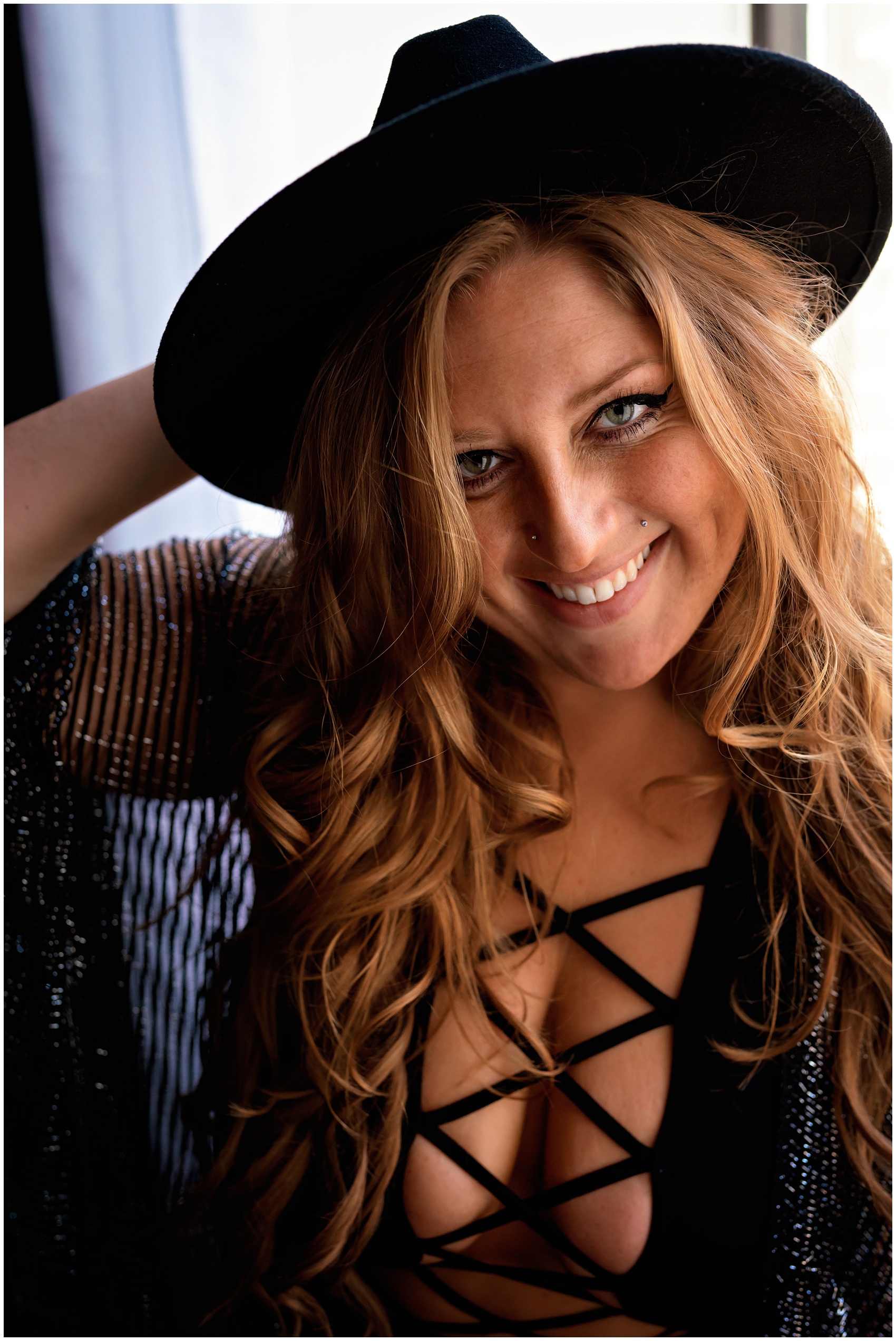 A woman smiles while wearing a black flat brimmed hat in a window