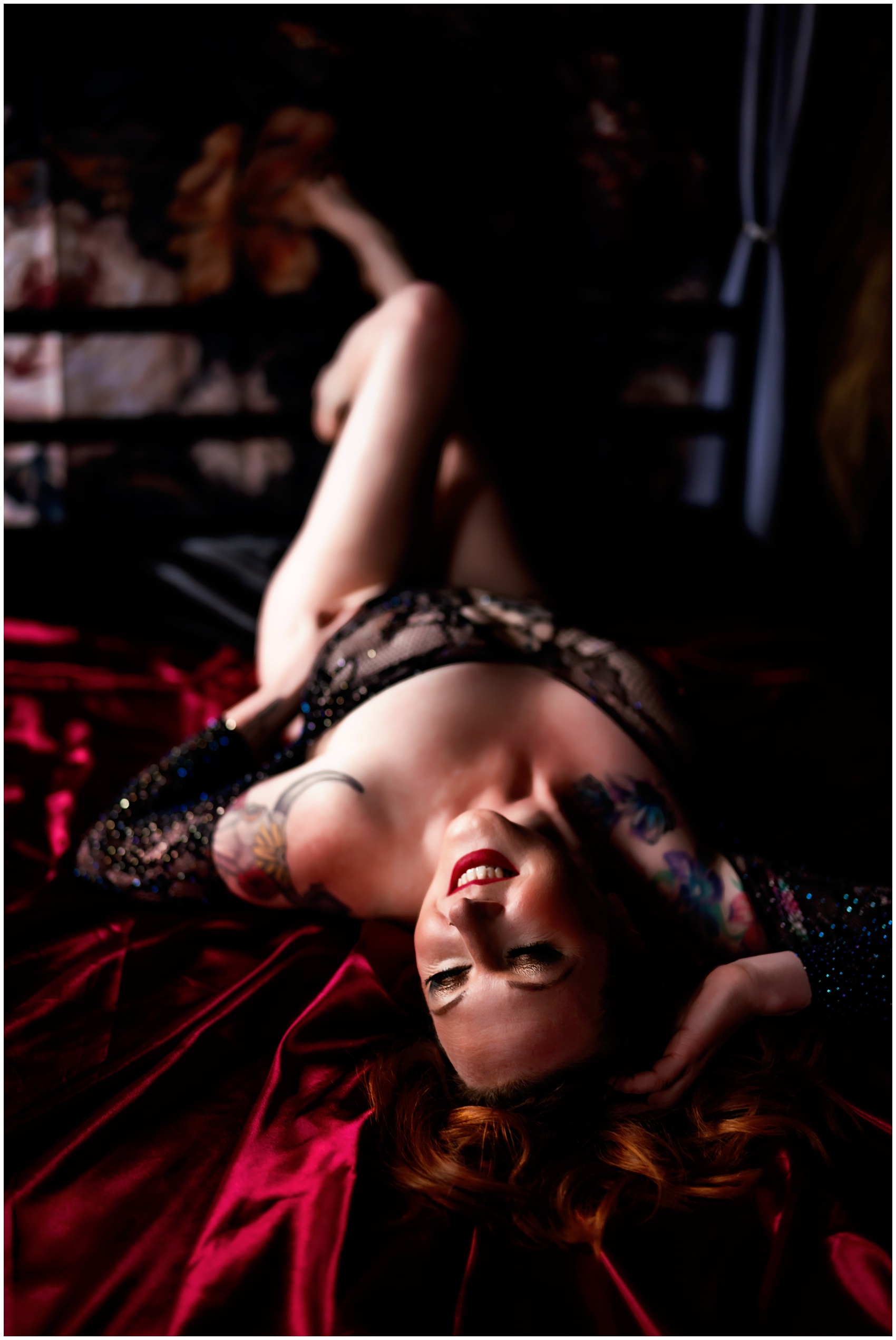 A woman in black mesh lingerie smiles while laying on a red bed after finding a personal trainer elgin